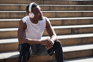 African american man take a break and listen online streaming music on smart phone after running workout. He sitting on  stair with relaxing feeling. Bodybuilding and exercise concept.