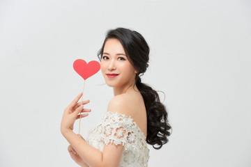 Asian woman in a wedding dress is holding  red heart on stick on a white background in the studio