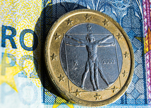 primo piano dell'uomo vitruviano rappresentato sul retro di una moneta da 1 euro, su sfondo una banconota da 20 euro