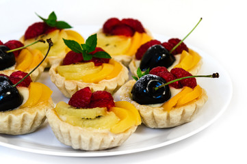 close up side view of a plate of fruit tartlets on a white surface