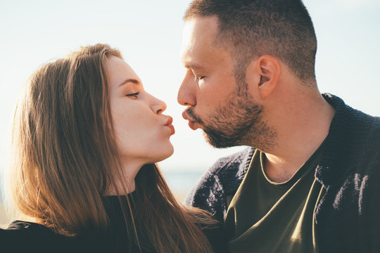 Man looking tenderly at woman and kissing. Young couple stands embracing. Family in love, sincere feelings of male and female. Waterfront. Close up portrait of beautiful people