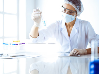 Professional female scientist in protective eyeglasses researching tube with reagents in laboratory. Concepts of medicine and science researching