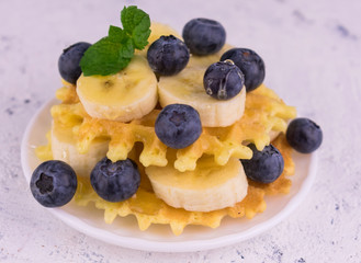 Waffles with berries and banana in a plate on a white background. Close-up.