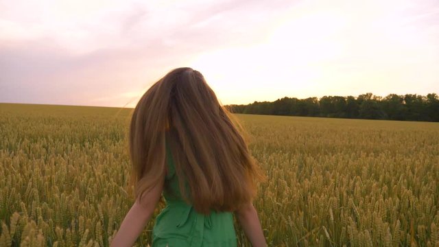 A beautiful teenager runs through a green field. Long hair develops in the wind. A girl in a green dress enjoys life, clean air. A happy child runs forward to a dream, rejoicing in a new day.