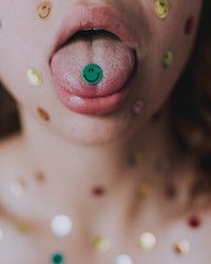 Vertical shot of a caucasian girl with smiley face stickers all over, with one on her tongue