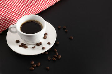 hot black coffee in white coffee cup and saucer with beans coffee and red fabric on black background.front view.