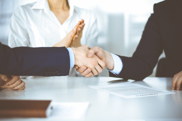 Business people shaking hands at meeting or negotiation, close-up. Two unknown businessmen and a woman sitting at the desk in a modern office. Teamwork, partnership and handshake concept