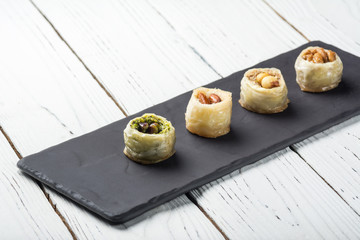 Turkish baklava, oriental sweets on a black dish for serving on a wooden white table. Horizontal format.