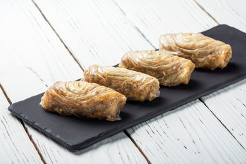 Turkish baklava, oriental sweets on a black dish for serving on a wooden white table. Food photo.