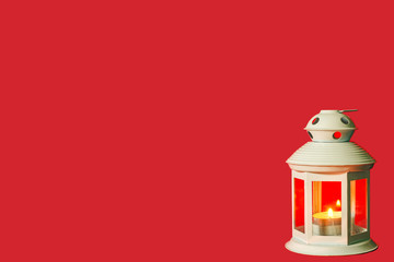 christmas white lantern with burning tea light on red background with space for text on the left