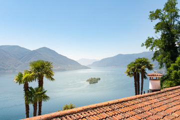 View over a Mediterranean roof with a fireplace between palm trees to Lake Maggiore and the Isola...