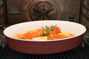 Juicy chicken drumsticks with sprig of rosemary in the oven in a baking dish with lemon halves.