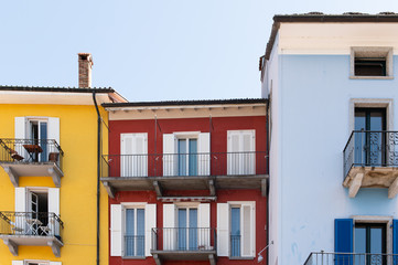 Colorful house front in the old town of Ascona in Switzerland in yellow, red and blue with a bright blue sky.