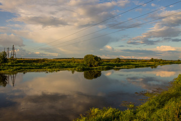 Pastoral landscape-Klyazma river Bank with green trees and grass against a blue cloudy sky with...