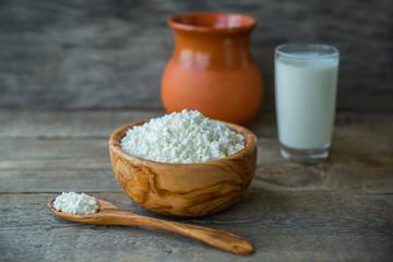 Fresh home-made curd in a wooden bowl on a linen napkin, with a glass of milk and a clay jug on a wooden old background.