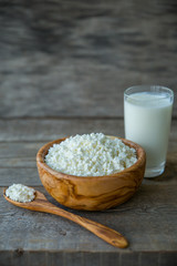 Fresh cottage cheese in a wooden bowl with a spoon with a glass of milk on a wooden old background