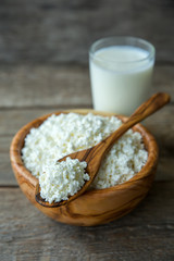 Fresh cottage cheese in a wooden bowl with a spoon with a glass of milk on a wooden old background