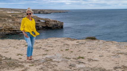 Happy lady in a yellow shirt young with a kind look blue clouds during the day and in the summer on a rocky beach