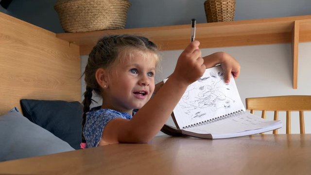 little girl draws in a notebook in a cafe