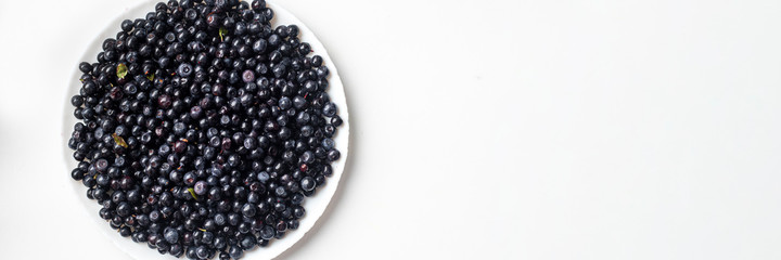 Blue delicious blueberries in a white plate on a white background top view