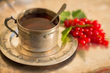 Obraz na płótnie Canvas An old beautiful silver cup of tea on a tray with red currants.
