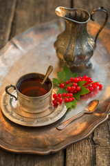 An old beautiful silver cup of tea on a tray with red currants.
