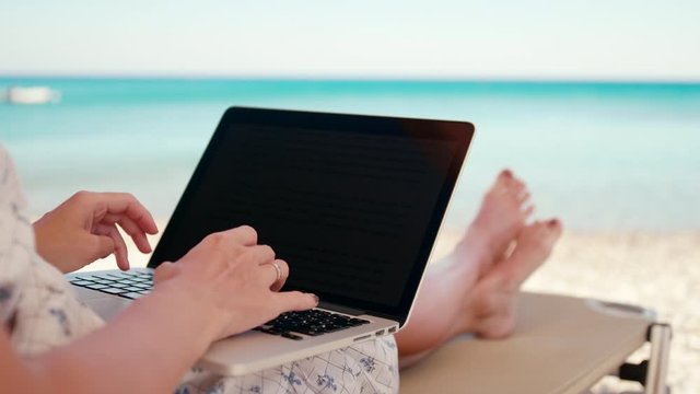 Woman Works Using Laptop on Sea Beach Sunbed in Summer. Unrecognizable Young Lady on Vacation with PC. Female Freelancer or Remote Worker. 4K Handheld Close up Shot
