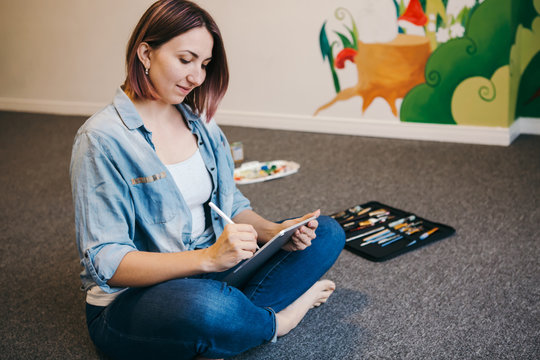 Lifestyle creative hobby and freelance artistic work job concept. Caucasian woman artist illustrator painting drawing on a touch pad digital tablet with stylus. Process of creating illustration.