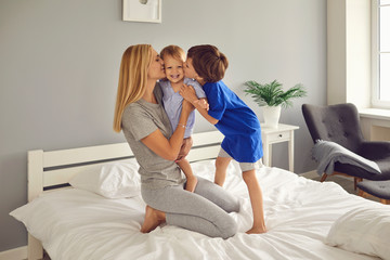 Mother and children hug and kiss on the bed in the room. Mothers Day. Mom and sons cuddle up.