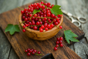 Ripe red currant berries in a wooden bowl on an old wooden table. Harvest.