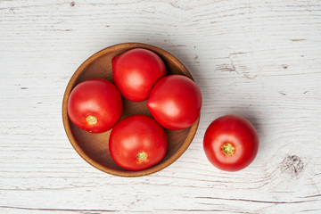 Top view of fresh raw tomatoes in wooden bowl on light wooden background
