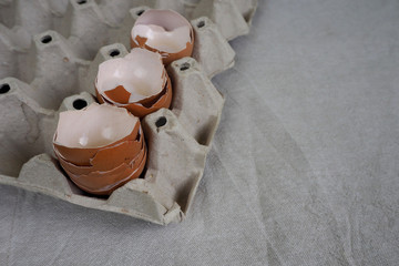 close up an empty shell with four eggs in a cardboard container side view against a gray linen tablecloth . food preparation