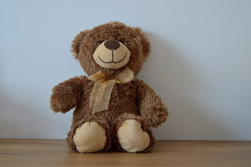 A small, sweet, brown teddy bear sits on a wooden table.