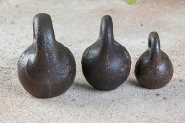 Three antique iron weights for scales on concrete background.