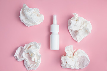 Nasal spray bottle and crumpled handkerchiefs on a pink background
