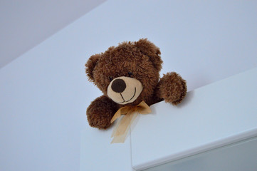 A brown teddy bear smiling hanging on the door and looking.