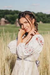 Portrait beautiful young woman with braided hair in white folk shirt enjoy summer nature and freedom, smile on wheat field. Happy attractive girl in embroided dress relax on countryside farmland