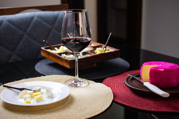 Wine and cheese. Wooden cheese board with gouda cheeses, fresh parmesan, parmesan and gorgonzola, served with red wine on a black topped table