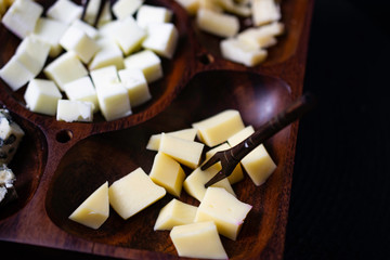 Wooden cheese board with gouda cheeses, fresh parmesan, parmesan and gorgonzola,  on a black topped table.
