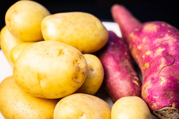 English potato and purple sweet potato in a white plate on a black table.