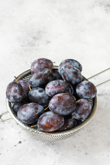 Ripe plum. Lots of plums in a metal bowl on a light background. Blue plums close-up. Healthy fruits	