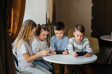 Children sit at a table in a cafe and play mobile phones together. Modern entertainment