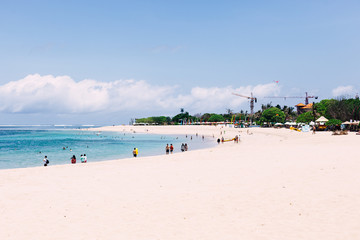 Nusa Dua beach with walking tourists in sunny day.