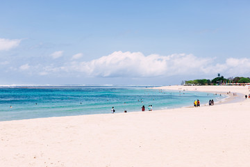 Nusa Dua beach with walking tourists in sunny day. 
