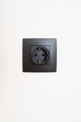 Black electric power plug socket on white wall. Modern interior design. Electricity in new appartment.  