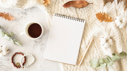 Autumn notes mockup. Flat lay composition with a spiral notebook, cup of coffee over knitted sweater with cotton and autumn leaves