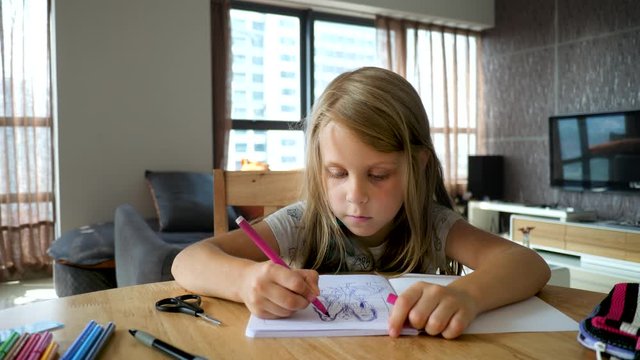 Cute Kid Girl Sitting At Wooden Table In Spacious Room And Drawing Picture With Colorful Markers In Sketch Book. Early Childhood Education Concept