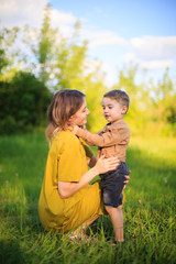 Fototapeta premium Cute baby boy and mother hug each other on green lawn. Summertime photography for ad or blog about motherhood