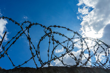 Spirals of barbed wire against a blue sky and clouds. wire fence