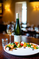 Mussel salad on a white plate with glass and bottle of wine on the background of the bar. Concept of a beautiful dish serving for a restaurant.